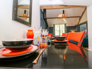 A dining table set with bowls plates glasses and cutlery with orange chairs in a room with wooden beams at The Hemmel in Faringdon