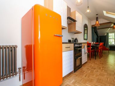 A kitchen with an orange fridge a stove wooden cabinets and a dining table with red chairs at The Hemmel in Faringdon