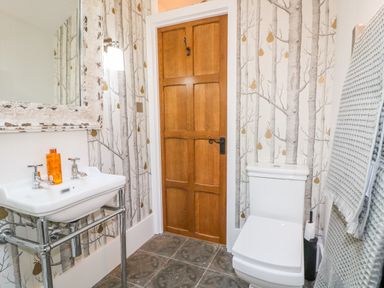 A bathroom with a white sink and toilet wooden door and tree patterned wallpaper at The Hemmel in Faringdon