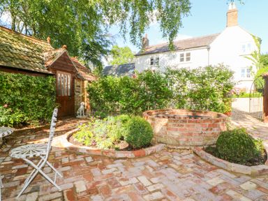 A garden patio with brick paving a circular brick fire pit greenery and a small shed at The Hemmel in Faringdon
