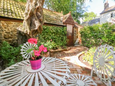 Outdoor garden area with white metal table and chairs with a potted pink flower and brick pathway at The Hemmel in Faringdon
