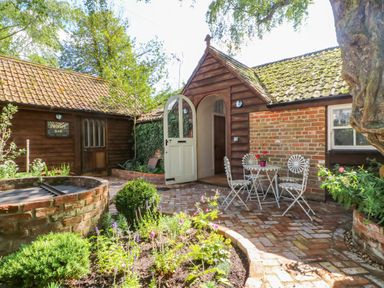 A garden courtyard with a circular brick planter and white metal table and chairs at The Hemmel in Faringdon