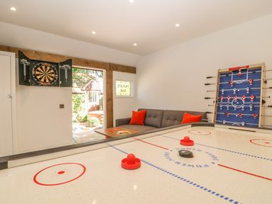 A game room with an air hockey table dartboard foosball table and a sofa with red cushions at The Hemmel in Faringdon