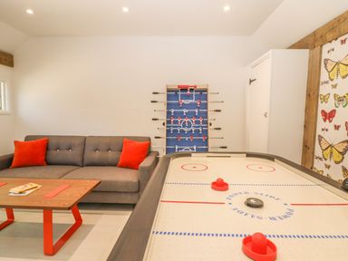 A game room with an air hockey table a foosball table a gray sofa with orange pillows and a wooden table at The Hemmel in Faringdon