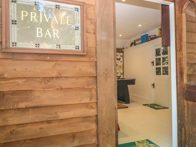 An entrance to a private bar with wooden walls and a door showing a room with a pool table and butterfly wallpaper at The Hemmel in Faringdon