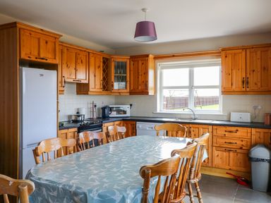 A kitchen with wooden cabinets a dining table with chairs and appliances at Doornogue in Churchtown near Fethard-on-Sea