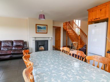 A dining table with wooden chairs a leather sofa a fireplace wooden stairs and a refrigerator at Doornogue Churchtown near Fethard-on-Sea