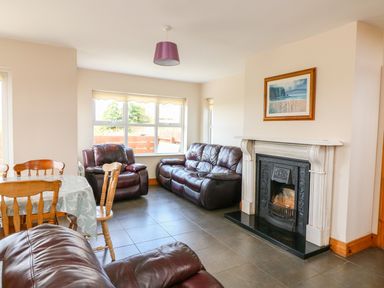 A living room with brown leather sofas a dining table with chairs and a fireplace with a painting above it at Doornogue in Churchtown near Fethard-on-Sea