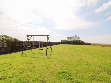 A backyard with a swing set and wooden fences surrounding it with a house in the background at Doornogue in Churchtown near Fethard-on-Sea