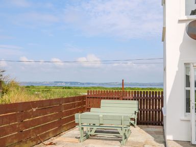 An outdoor patio area with wooden benches and a wooden fence overlooking a landscape with fields and water at Doornogue in Churchtown near Fethard-on-Sea