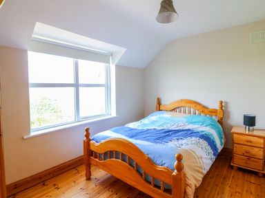 A bedroom with a wooden bed and nightstand next to a window at Doornogue in Churchtown near Fethard-on-Sea