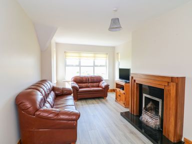 A living room with two brown leather sofas a wooden fireplace and a TV on a wooden cabinet at Doornogue in Churchtown near Fethard-on-Sea