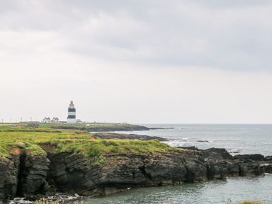 A coastal scene with rocky cliffs grassy areas and a striped lighthouse at Doornogue Churchtown near Fethard-on-Sea