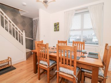 A dining room with a wooden table and six chairs near a window with white curtains at Yr Adfa The Retreat in Blaenau Ffestiniog