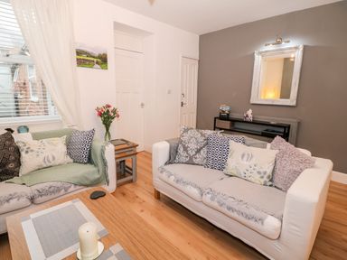 A living room with two sofas pillows a wooden coffee table with candle flowers on a side table and a mirror on the wall at Yr Adfa The Retreat in Blaenau Ffestiniog