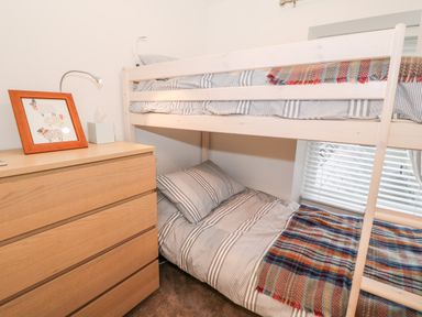 A bedroom with wooden bunk beds striped bedding a wooden dresser with framed artwork and a tissue box at Yr Adfa The Retreat in Blaenau Ffestiniog