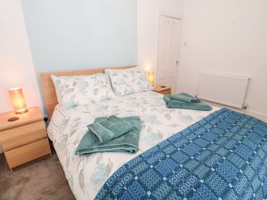 A bedroom with a double bed with floral bedding blue towels on the bed two wooden bedside tables with lamps and a white door at Yr Adfa The Retreat in Blaenau Ffestiniog
