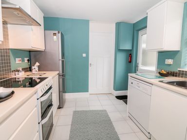 A kitchen with white cabinets teal walls a refrigerator stove dishwasher and a door at Yr Adfa The Retreat in Blaenau Ffestiniog
