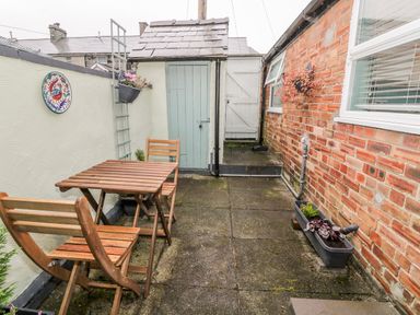 A small patio with a wooden table and two chairs next to light blue door and brick wall at Yr Adfa The Retreat in Blaenau Ffestiniog