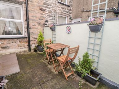An outdoor patio with a wooden table and two chairs stone walls planters with plants and flower pots at Yr Adfa (The Retreat) in Blaenau Ffestiniog