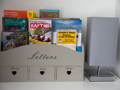 A collection of travel guides and maps in a letters holder next to a table lamp at Yr Adfa The Retreat in Blaenau Ffestiniog