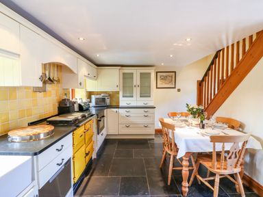 A kitchen with white cabinets yellow appliances a dining table set with plates and glasses and wooden stairs at Great Bradley Cottage in Withypool