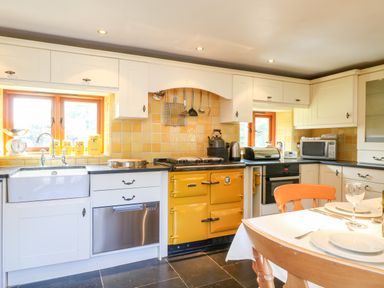 A kitchen with yellow tiled walls white cabinets a yellow stove and a wooden dining table with chairs at Great Bradley Cottage in Withypool