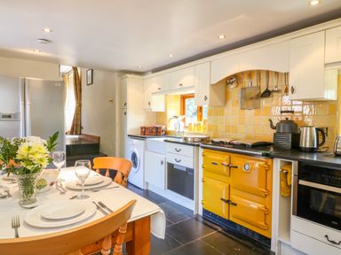 A kitchen with a yellow stove dishwasher and dining table with chairs at Great Bradley Cottage in Withypool