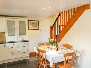 A dining table set for four near wooden stairs in a kitchen with white cabinets at Great Bradley Cottage in Withypool