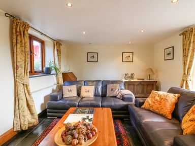 A living room with leather sofas a wooden coffee table with decorative bowl a sideboard with a lamp and framed pictures on the wall at Great Bradley Cottage in Withypool