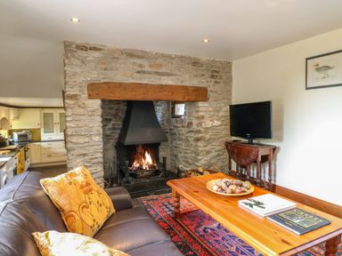 A living room with a stone fireplace and a wooden coffee table with books and decorative items at Great Bradley Cottage in Withypool