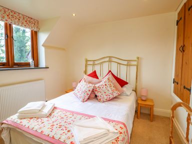 A bedroom with a bed with floral bedding and pillows beside windows and wooden furniture at Great Bradley Cottage in Withypool