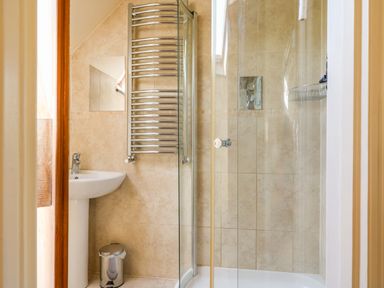 A bathroom with a pedestal sink a wall-mounted towel radiator a glass-enclosed shower and a small trash bin at Great Bradley Cottage in Withypool