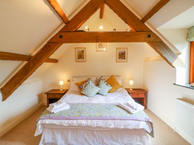 A bedroom with a double bed wooden beams and bedside tables with lamps at Great Bradley Cottage in Withypool