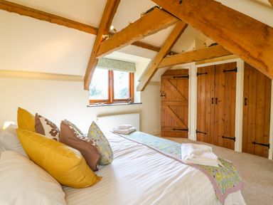 A bedroom with a bed and pillows under wooden beams with wooden closets at Great Bradley Cottage in Withypool