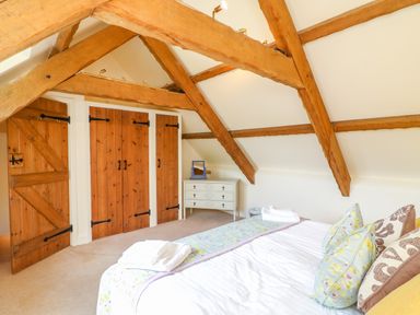 A bedroom with exposed wooden beams wooden doors a bed with pillows and folded towels and a white dresser at Great Bradley Cottage in Withypool
