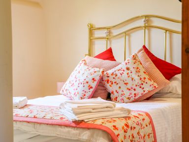A bed with floral pillows and folded towels on a bedspread at Great Bradley Cottage in Withypool