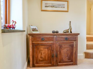 A wooden cabinet with framed photo sculpture and decorative items next to a window in a hallway at Great Bradley Cottage in Withypool