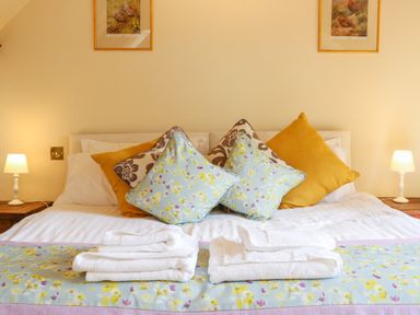A bedroom with a bed with multiple pillows and folded towels on a floral runner at Great Bradley Cottage in Withypool