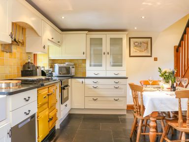 A kitchen with white cabinets a yellow stove a microwave and a dining table set with glasses and flowers at Great Bradley Cottage in Withypool