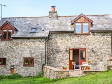 Stone cottage with multiple windows and a patio with outdoor furniture and potted plants at Great Bradley Cottage in Withypool