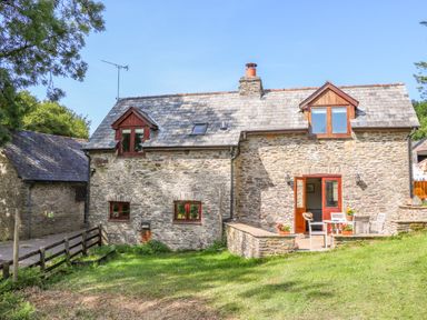 A stone cottage with wooden framed windows and a patio with chairs and a table at Great Bradley Cottage in Withypool
