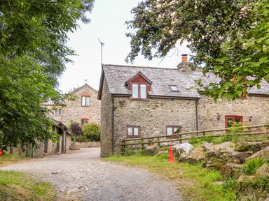 Stone cottages surrounded by trees and plants with a gravel path and a traffic cone at Great Bradley Cottage in Withypool