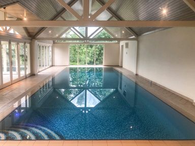 An indoor swimming pool with blue tiles and a glass wall with views of trees at Great Bradley Cottage in Withypool