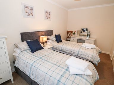 A bedroom with two single beds a bedside table with a lamp a chest of drawers a dressing table with a mirror and a wooden chair at 4 Ty Rhosyn in Morfa Bychan