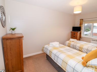 A bedroom with two single beds with plaid bedding and wooden furniture at 4 Ty Rhosyn in Morfa Bychan