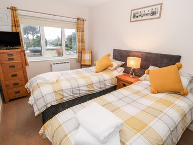 A bedroom with two single beds wooden chest of drawers and a window at 4 Ty Rhosyn Morfa Bychan