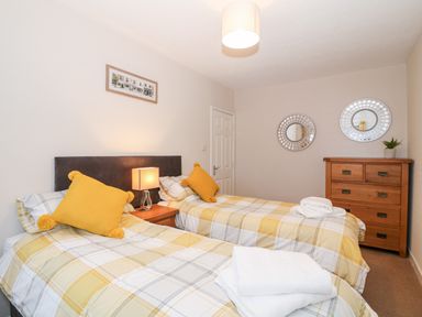 A bedroom with two single beds yellow pillows and a wooden dresser at 4 Ty Rhosyn in Morfa Bychan