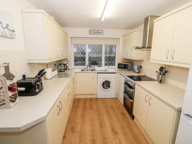 A kitchen with cream cabinets a washing machine a stove toaster and a window above the sink at 4 Ty Rhosyn Morfa Bychan