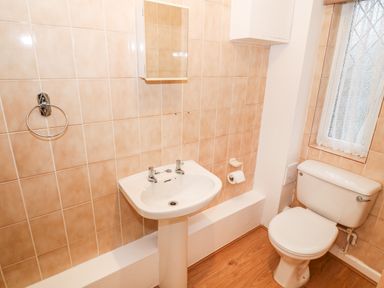 A bathroom with a pedestal sink toilet and a window with lace curtains at 4 Ty Rhosyn in Morfa Bychan
